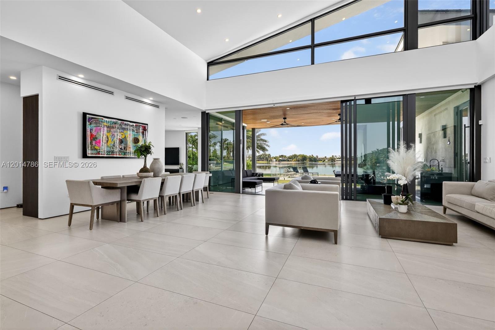 A modern open-concept living and dining area features high ceilings, large glass doors, and tile flooring — 1830 NE 193rd St, Miami FL 33179, MIAMI, FL
