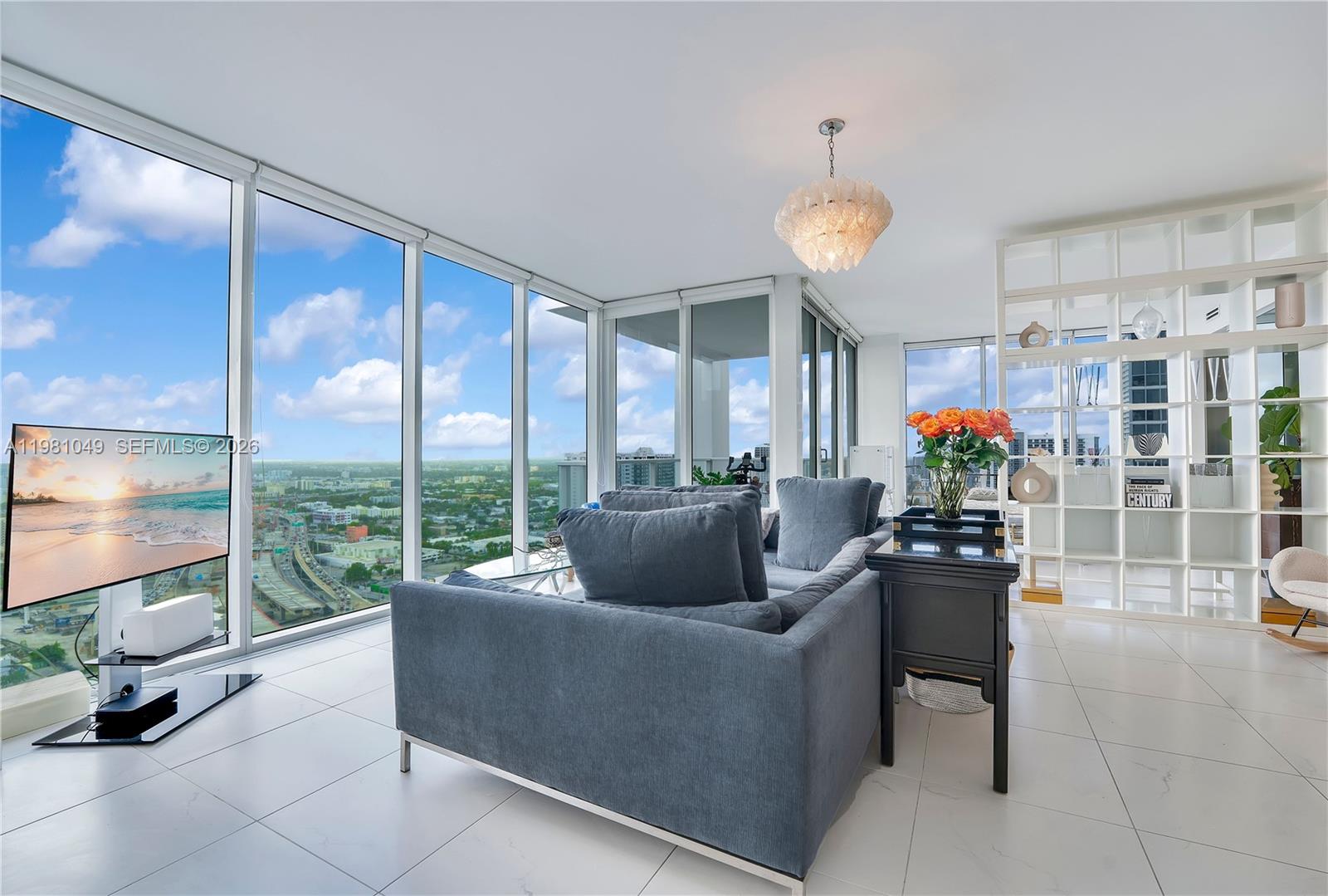 A modern living room features floor-to-ceiling windows, white tile flooring, and a gray sofa — 1040 Biscayne Blvd # 3306, Miami FL 33132, MIAMI, FL