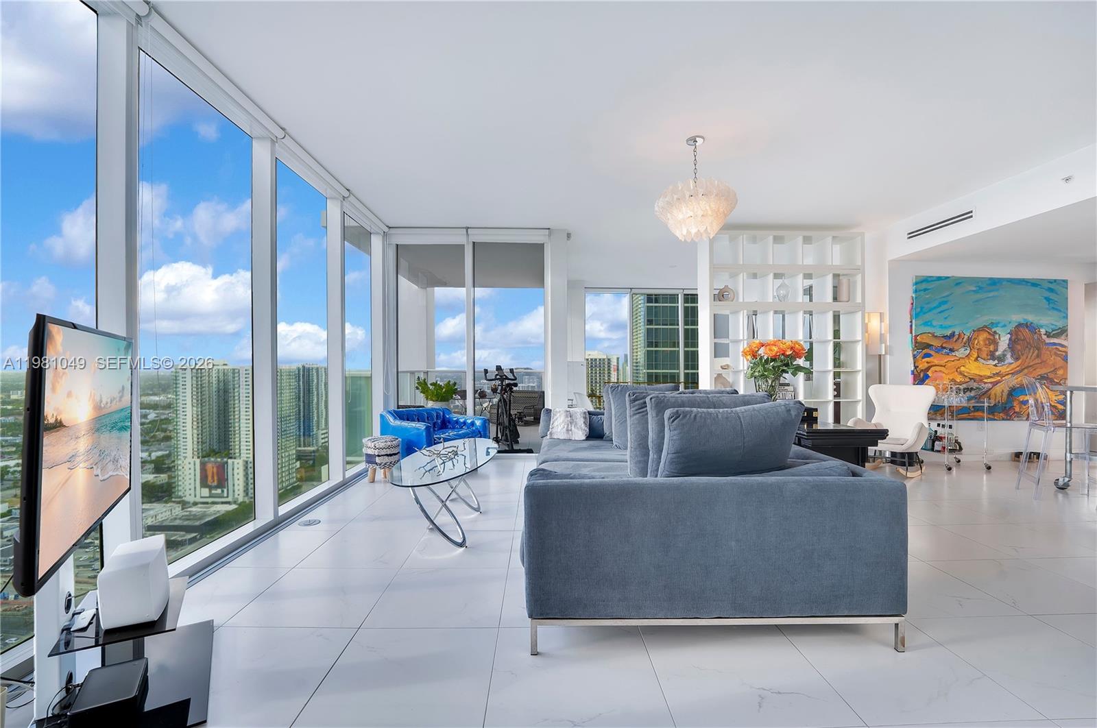 A modern living room features floor-to-ceiling windows, white tile floors, and a blue sofa — 1040 Biscayne Blvd # 3306, Miami FL 33132, MIAMI, FL