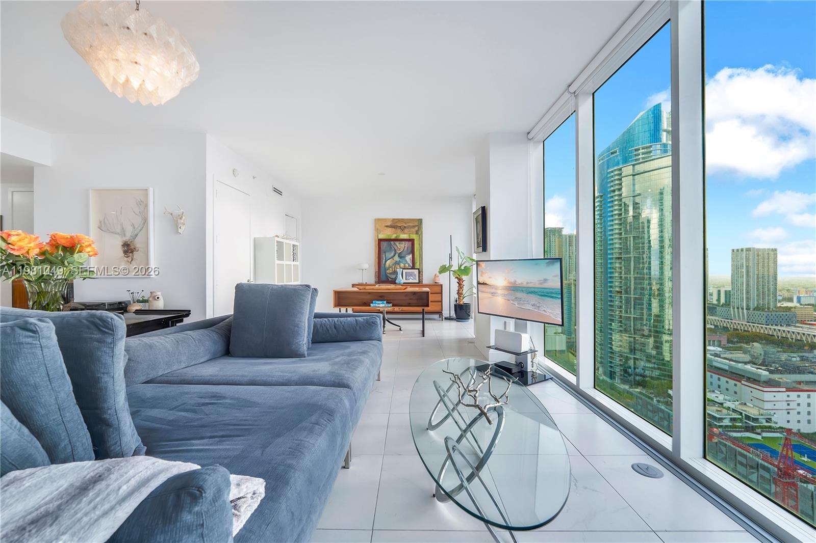 A modern living room features a blue sofa, glass coffee table, and floor-to-ceiling windows — 1040 Biscayne Blvd # 3306, Miami FL 33132, MIAMI, FL