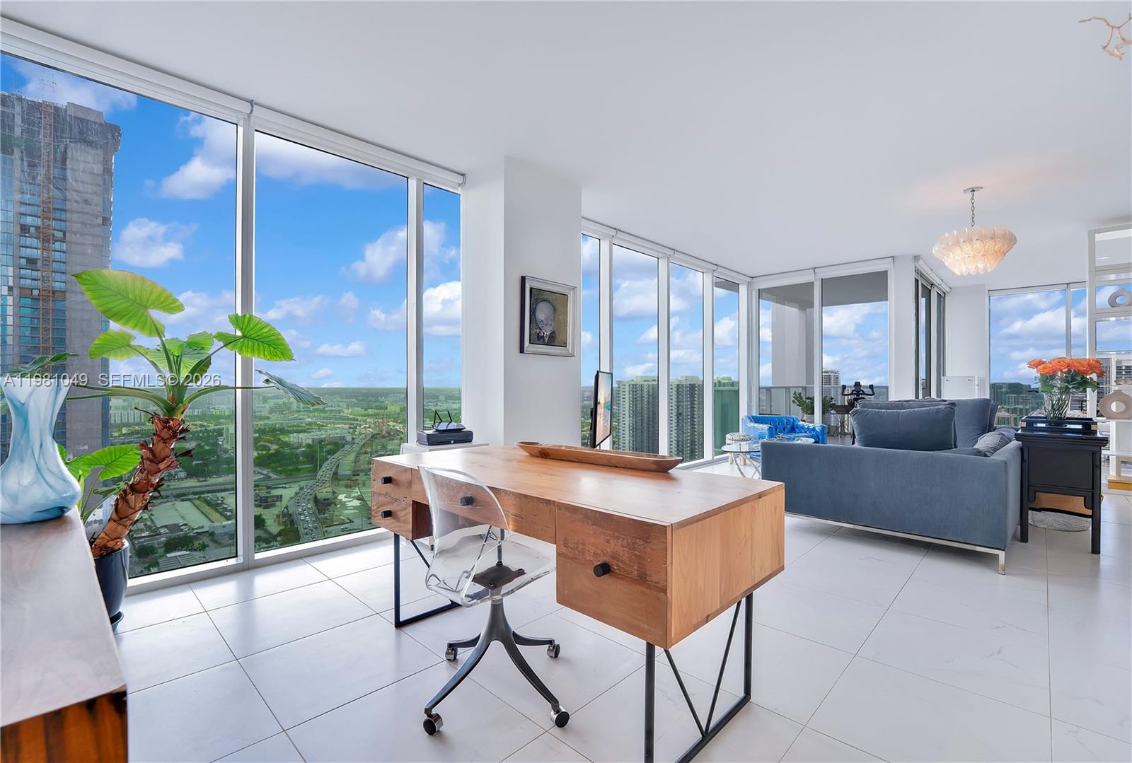 A modern home office features a wooden desk, acrylic chair, and floor-to-ceiling windows with city views — 1040 Biscayne Blvd # 3306, Miami FL 33132, MIAMI, FL
