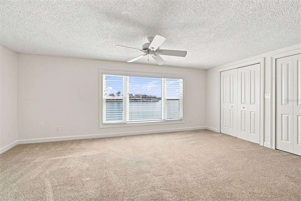 An empty bedroom with beige carpeting, a ceiling fan, and a window overlooking the water — 13155 BOCA CIEGA AVENUE, MADEIRA BEACH, FL