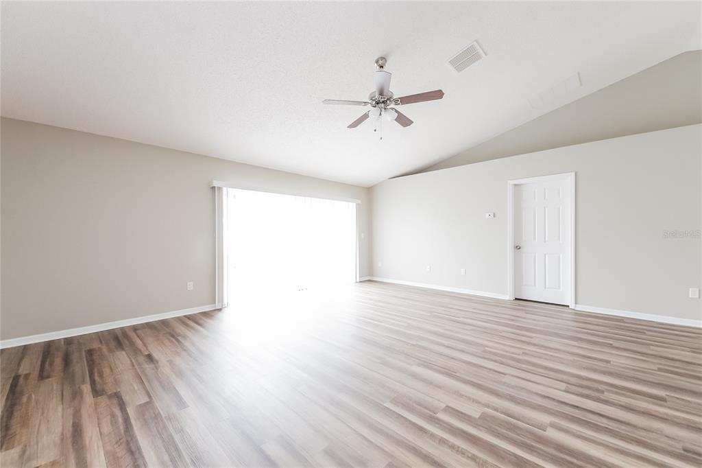 An empty living room features light-colored walls, wood-look flooring, a ceiling fan, and sliding doors — 826 SAN JOSE COURT, KISSIMMEE, FL