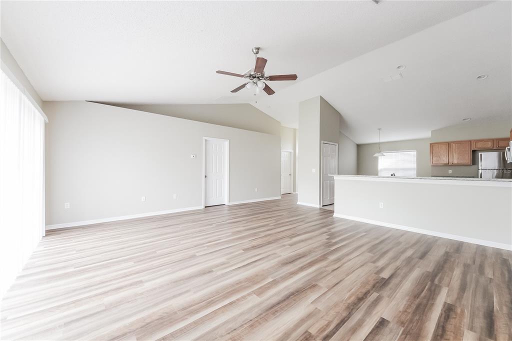 An open-concept living area features vaulted ceilings, wood-look flooring, and an adjacent kitchen — 826 SAN JOSE COURT, KISSIMMEE, FL