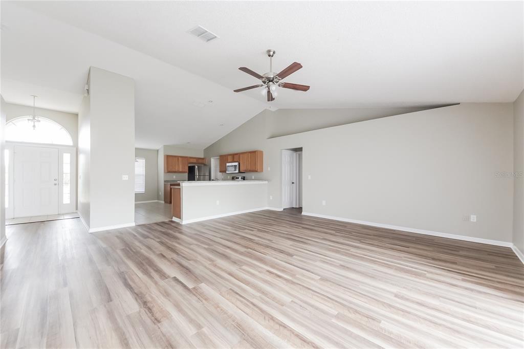 An open-concept living area features vaulted ceilings, wood-look flooring, and an adjacent kitchen with cabinets — 826 SAN JOSE COURT, KISSIMMEE, FL