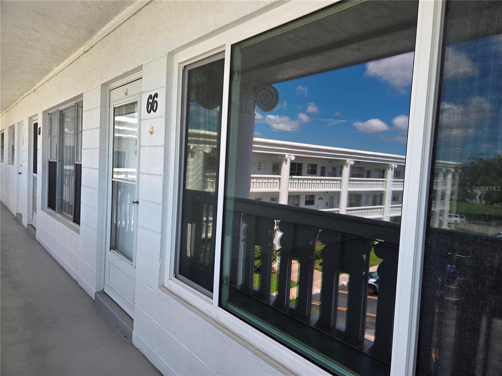 A white exterior walkway features a numbered door and a large window reflecting a building — 2454 AUSTRALIA WAY E UNIT 66, CLEARWATER, FL