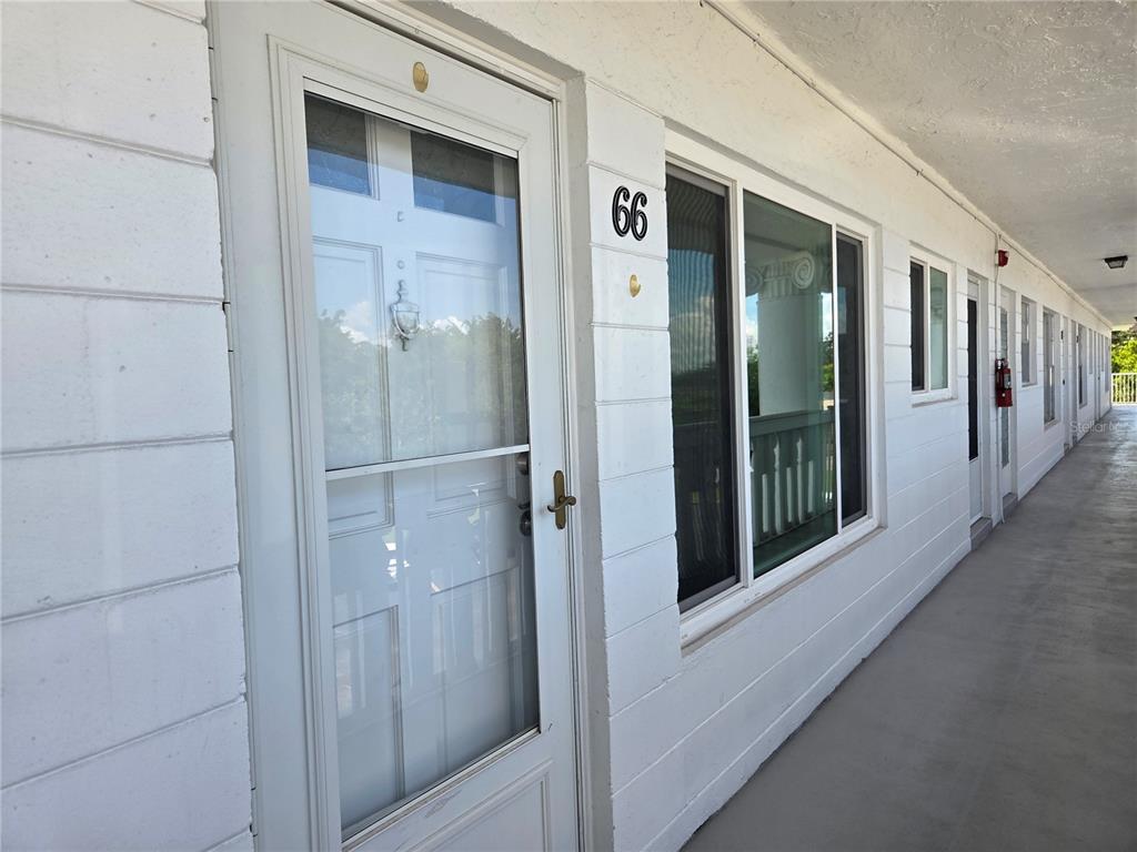 A white exterior hallway features a door marked with the number 66 and windows — 2454 AUSTRALIA WAY E UNIT 66, CLEARWATER, FL