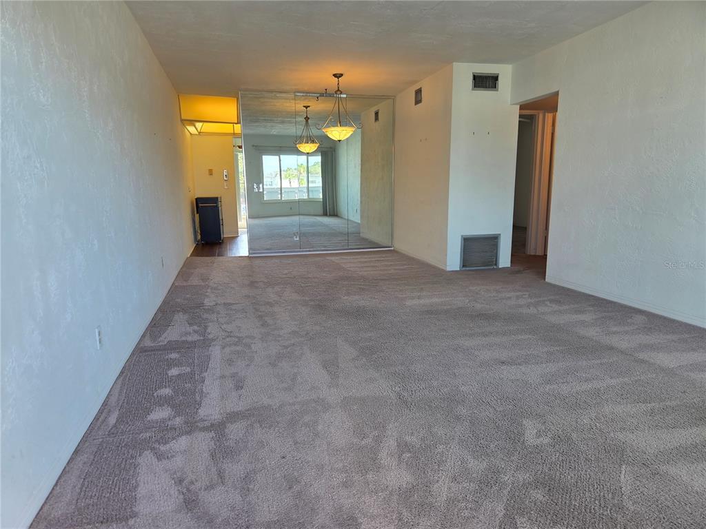 An empty living room features beige wall-to-wall carpeting, white walls, and a large mirrored wall — 2454 AUSTRALIA WAY E UNIT 66, CLEARWATER, FL