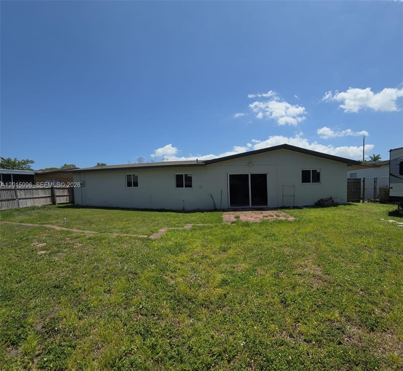 The rear exterior of a single-story house features a sliding glass door and a grassy yard — 11941 SW 200th St, Miami FL 33177, MIAMI, FL