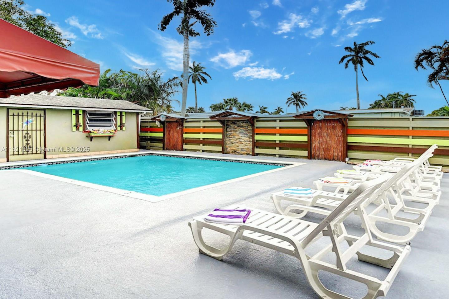 A swimming pool sits in a backyard with lounge chairs and a colorful wooden fence — 1020 N 13th Ter, Hollywood FL 33019, HOLLYWOOD, FL