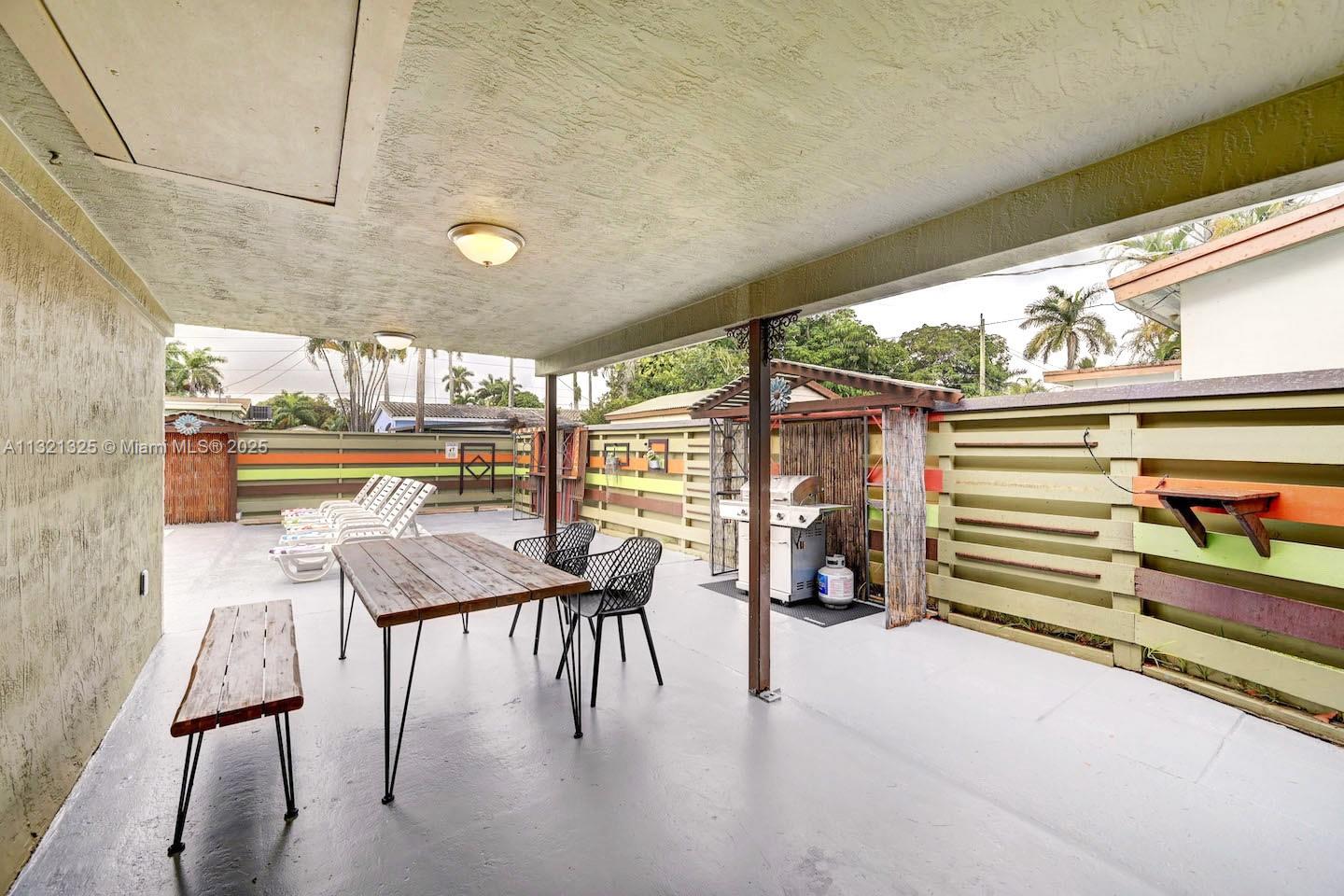 A covered outdoor patio features a wooden dining table, chairs, and a grill area — 1020 N 13th Ter, Hollywood FL 33019, HOLLYWOOD, FL