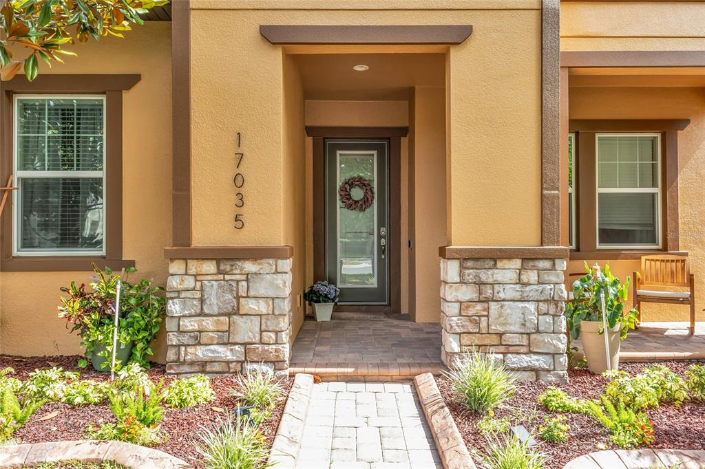 The front entrance of a house features a stone-accented facade, a paved walkway, and landscaping — 17035 HARBOR OAK PARKWAY, WINTER GARDEN, FL