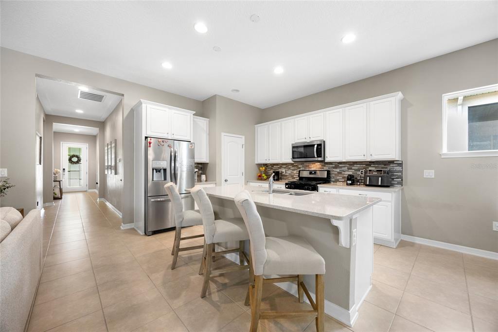 A kitchen features white cabinets, stainless steel appliances, a quartz island, and three bar stools — 17035 HARBOR OAK PARKWAY, WINTER GARDEN, FL