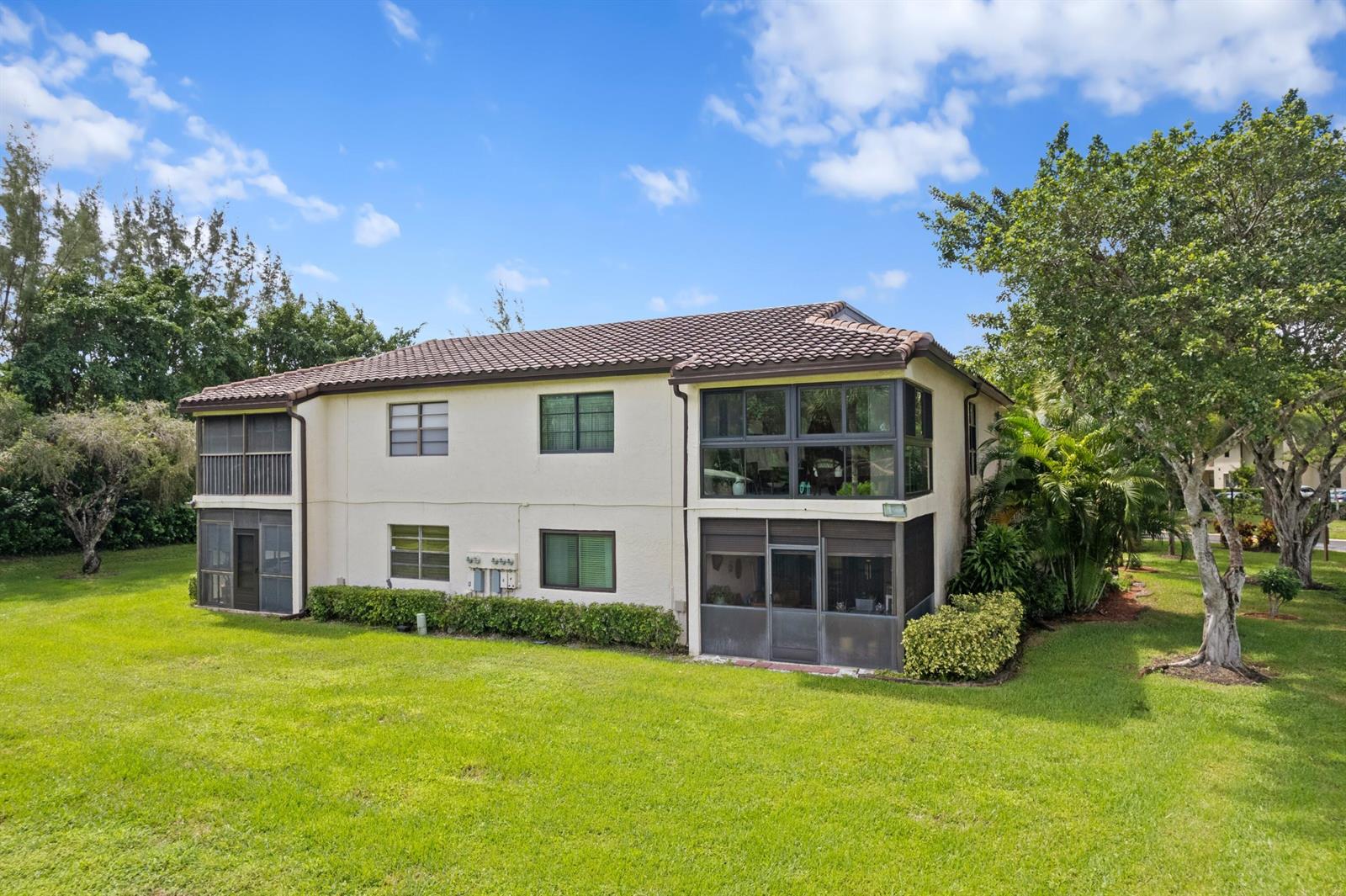 A two-story residential building with a tiled roof, screened balconies, and surrounding green lawn — 21734 Arriba Real # 32b, Boca Raton FL 33433, BOCA RATON, FL