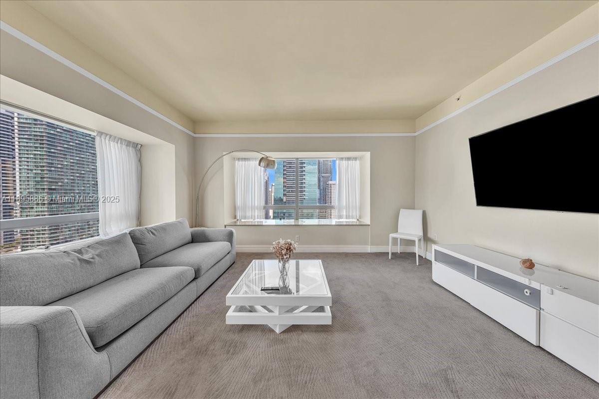 A living room features a gray sofa, white coffee table, media console, and city views — 1435 Brickell Ave # 3112, Miami FL 33131, MIAMI, FL