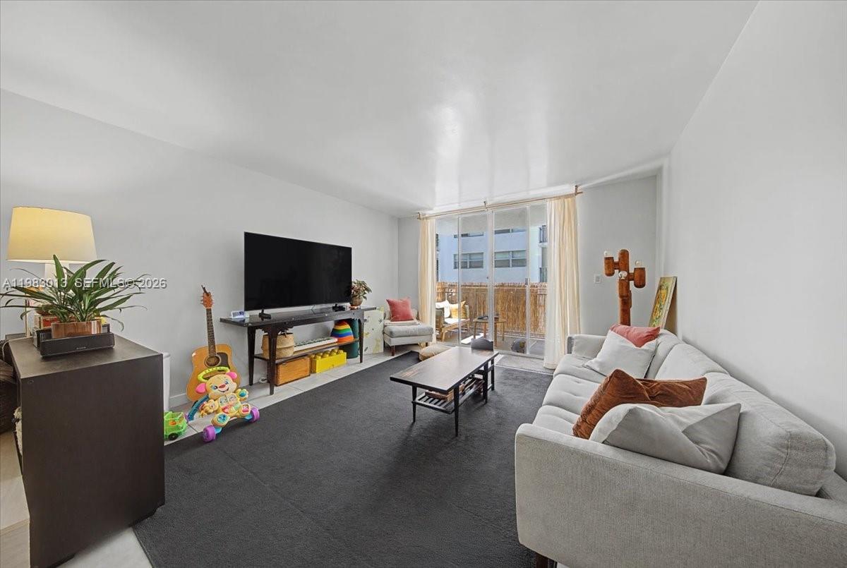 A living room features a gray sofa, a dark rug, a television, and a balcony door — 777 NE 62nd St # C211, Miami FL 33138, MIAMI, FL
