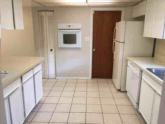 A kitchen features white cabinets, tile flooring, a wall oven, and a white refrigerator — 2730 PRINCE JOHN ROAD, WINTER PARK, FL