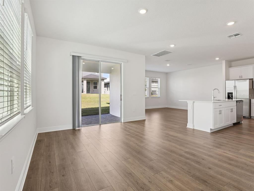 An open-concept living area features wood-look flooring, a kitchen island, and a sliding glass door — 2178 WILDBERRY ROAD, MINNEOLA, FL