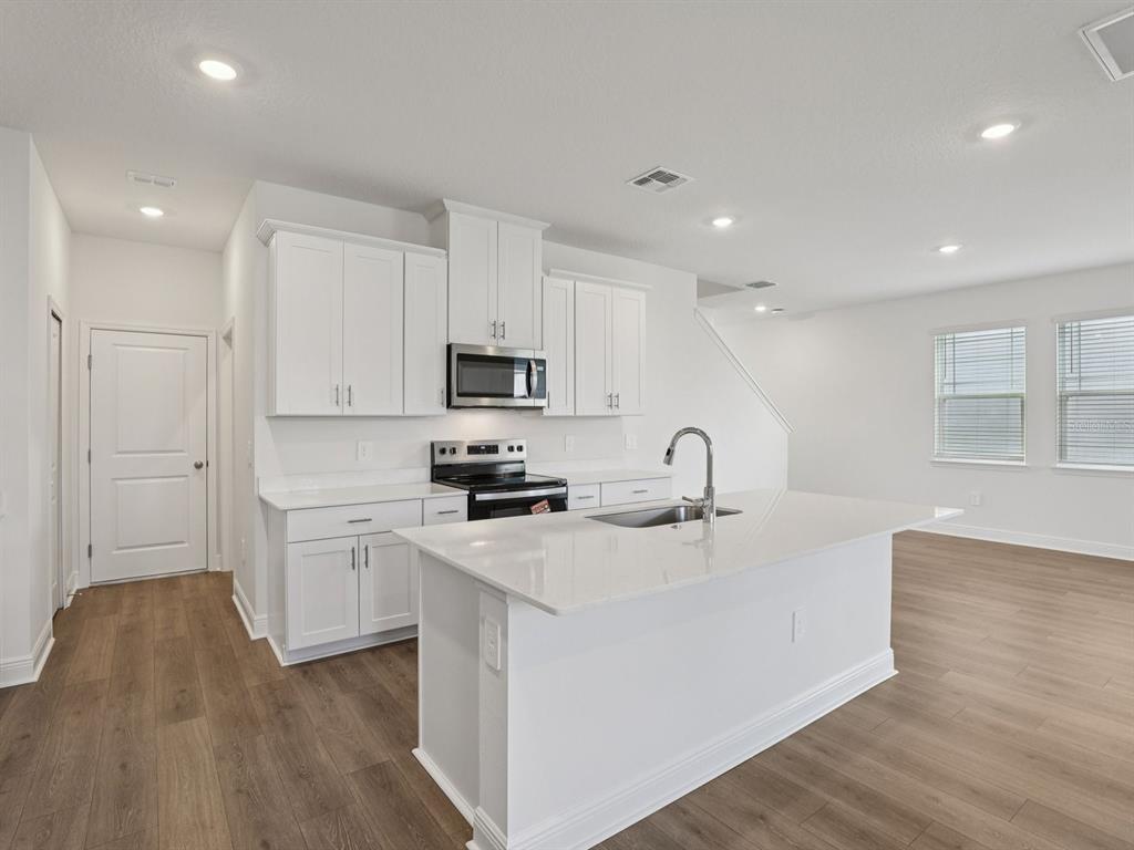 A modern kitchen features white cabinetry, a quartz island, and light wood-look flooring — 2178 WILDBERRY ROAD, MINNEOLA, FL