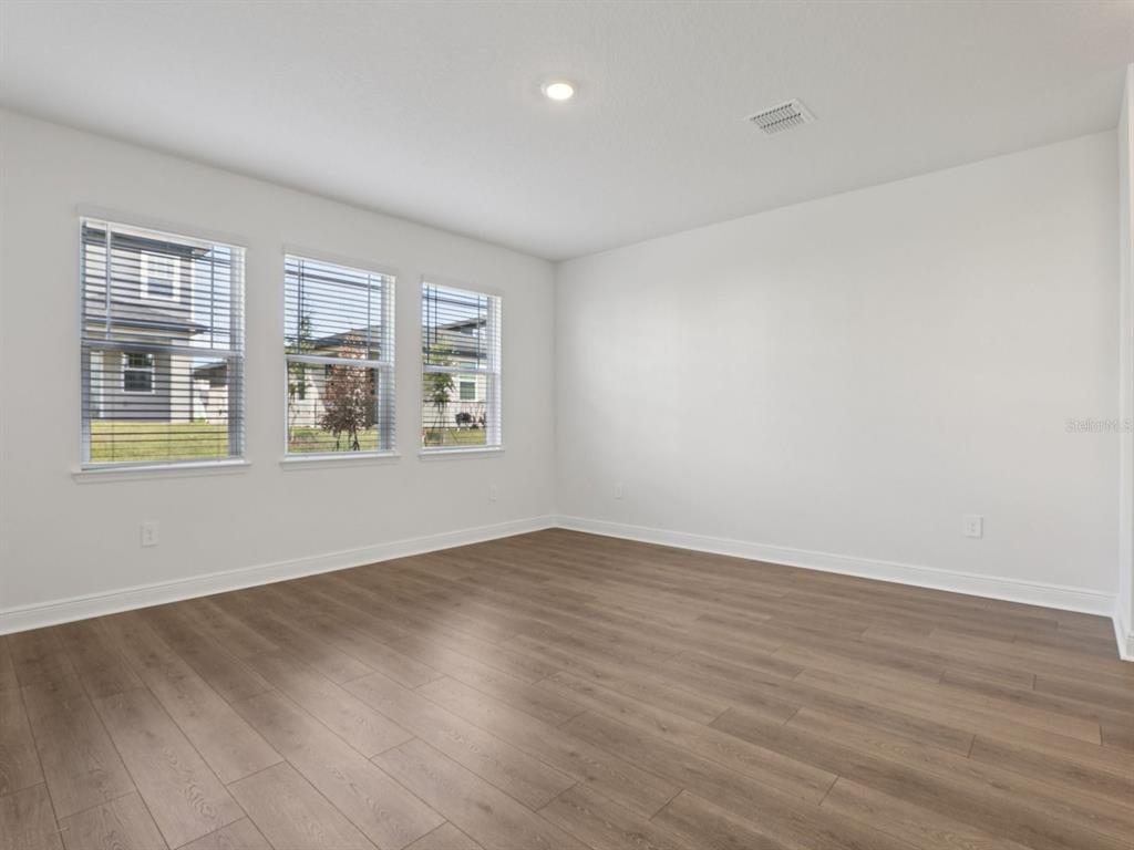 An empty room with white walls, wood-look flooring, and three windows with blinds — 2178 WILDBERRY ROAD, MINNEOLA, FL