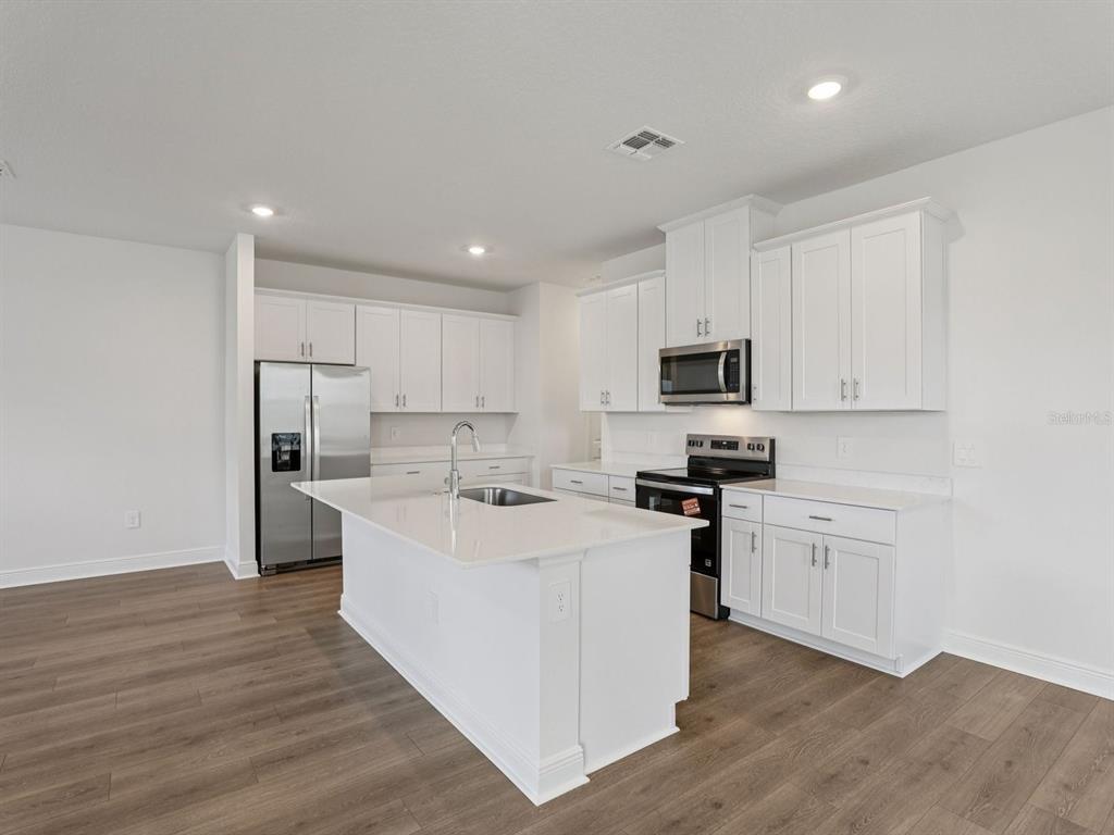 A modern kitchen features white cabinets, stainless steel appliances, a center island, and wood-look flooring — 2178 WILDBERRY ROAD, MINNEOLA, FL
