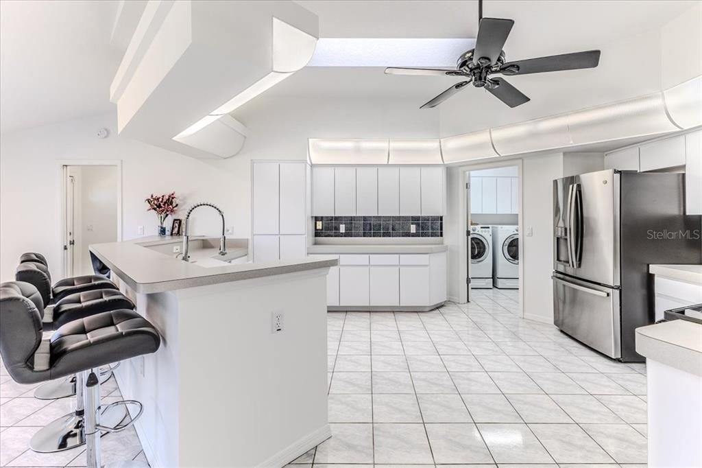 A bright kitchen features white cabinetry, a breakfast bar, stainless steel appliances, and tile flooring — 13377 BOLTON COURT, SPRING HILL, FL