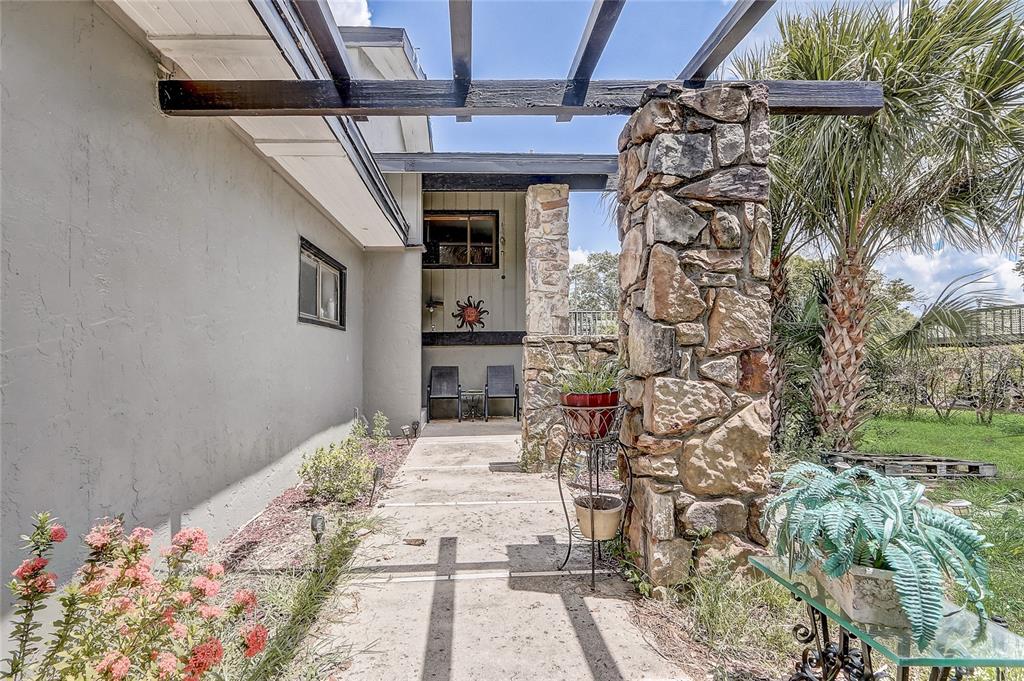 A stone pillar supports a wooden pergola over a concrete walkway leading to a patio — 32 NOTTINGHAM WAY, HAINES CITY, FL