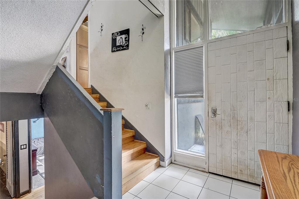 An entryway features a wooden staircase, white tile flooring, and a textured white front door — 32 NOTTINGHAM WAY, HAINES CITY, FL