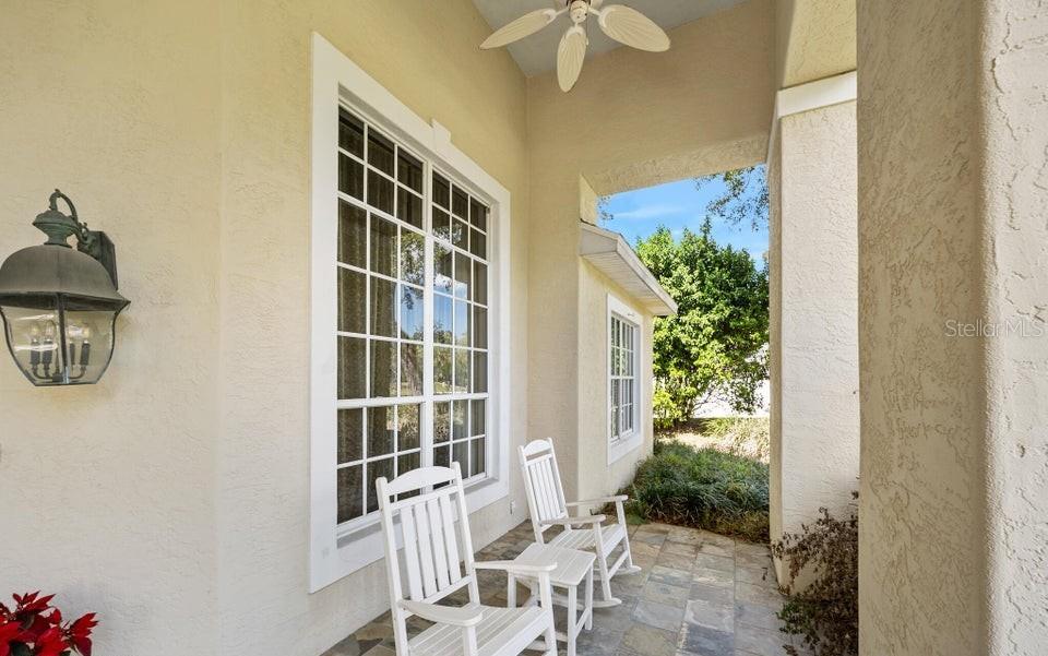 A covered porch features two white rocking chairs, a ceiling fan, and a stone floor — 6 BROADWATER DRIVE, ORMOND BEACH, FL