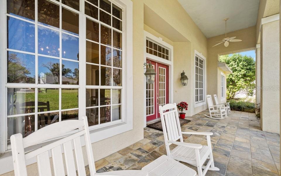 A covered porch features stone tile flooring, white rocking chairs, and a red double door — 6 BROADWATER DRIVE, ORMOND BEACH, FL