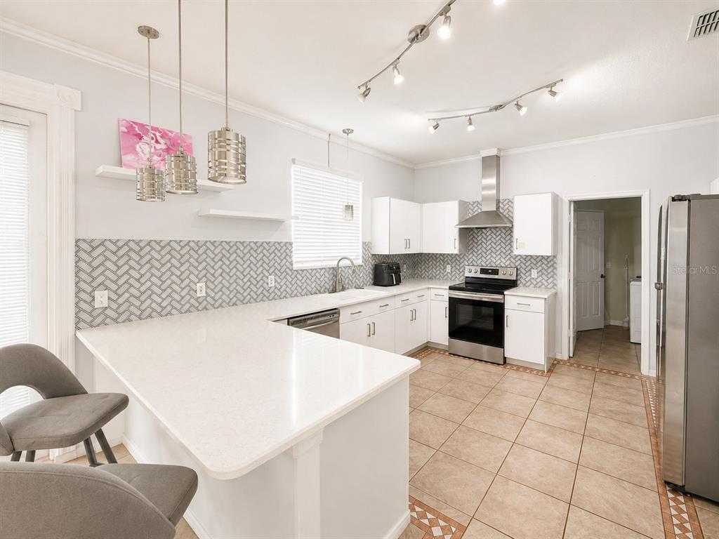A kitchen with white cabinets, a herringbone backsplash, stainless steel appliances, and a breakfast bar — 2808 PAYNES PRAIRIE CIRCLE, KISSIMMEE, FL