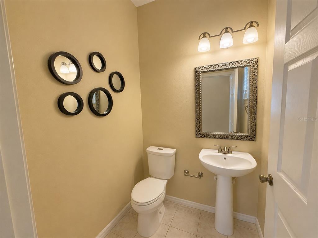 A small powder room features a pedestal sink, a toilet, and a decorative wall mirror — 2808 PAYNES PRAIRIE CIRCLE, KISSIMMEE, FL