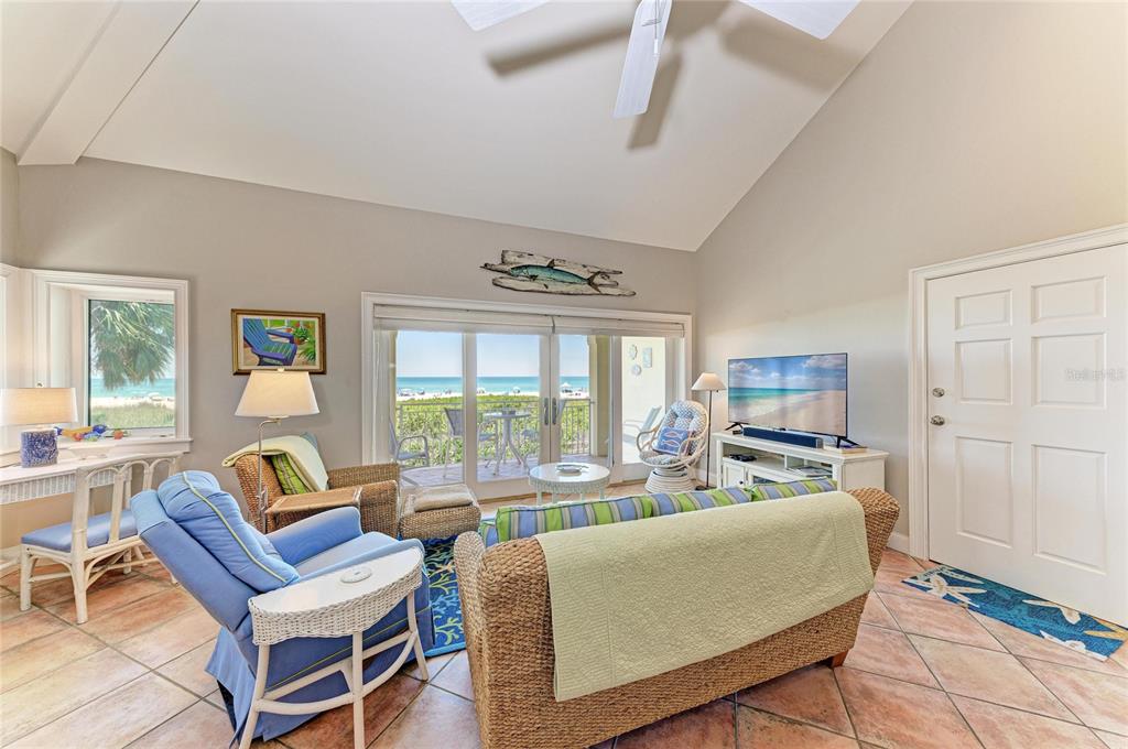 A living room features wicker furniture, tile floors, and sliding glass doors overlooking the ocean — 101 PALM AVENUE UNIT 3, ANNA MARIA, FL
