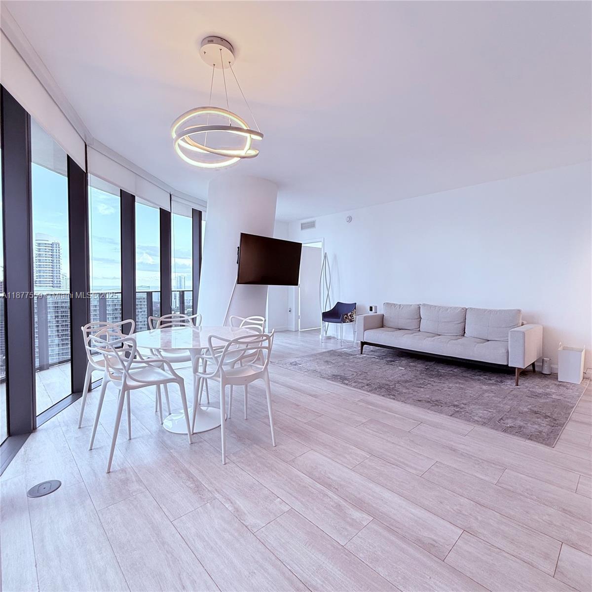 A modern living and dining area features floor-to-ceiling windows, light wood floors, and white walls — 55 SW 9th St # 4003, Miami FL 33130, MIAMI, FL