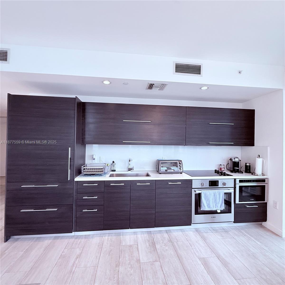 A modern kitchen features dark wood-grain cabinetry, stainless steel appliances, and light-colored flooring — 55 SW 9th St # 4003, Miami FL 33130, MIAMI, FL