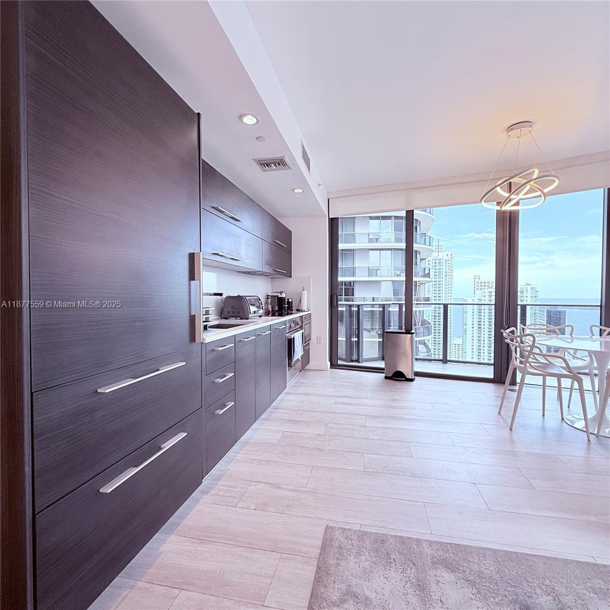 A modern kitchen with dark wood cabinetry and a dining area overlooking a city skyline — 55 SW 9th St # 4003, Miami FL 33130, MIAMI, FL