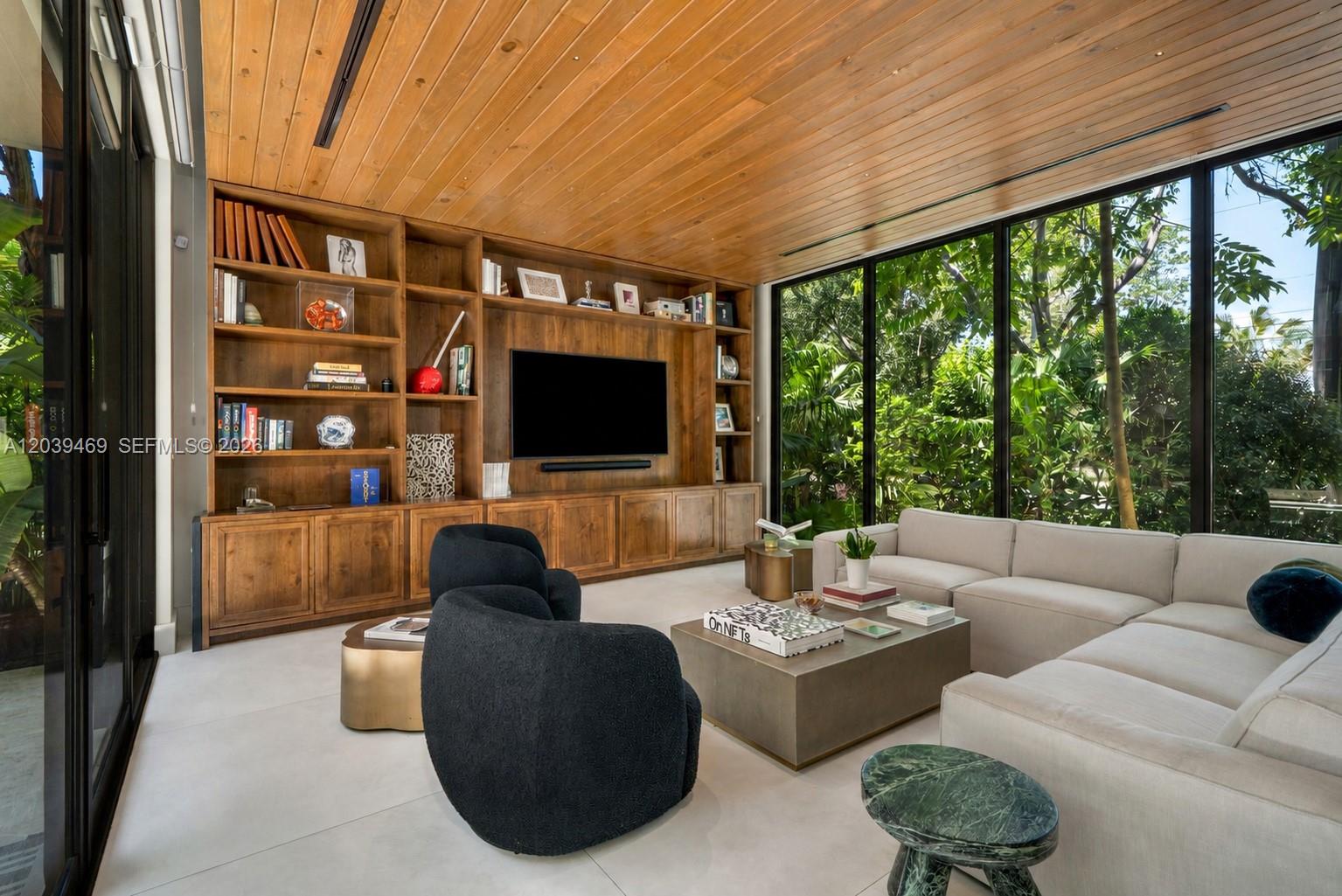 A modern living room features wood-paneled walls, built-in shelving, a large sofa, and floor-to-ceiling windows — 7851 SW 48th Pl, Miami FL 33143, MIAMI, FL