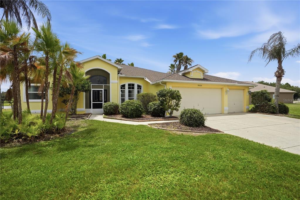 A yellow single-story house with a three-car garage and a screened front entryway — 18131 RIVARD BOULEVARD, BROOKSVILLE, FL