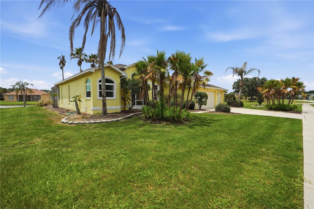 A yellow house with a palm-filled front yard and a driveway under a blue sky — 18131 RIVARD BOULEVARD, BROOKSVILLE, FL