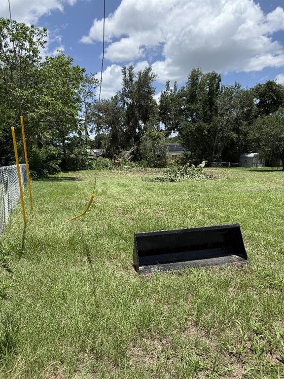 A grassy backyard features a detached tractor bucket, a chain-link fence, and mature trees — 5427 SE 137TH LANE, SUMMERFIELD, FL
