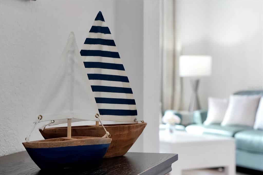 Two decorative wooden sailboat models sit on a dark surface in a blurred living room — 4862 CAYVIEW AVENUE UNIT 102, ORLANDO, FL