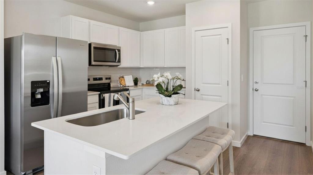 A kitchen features white cabinets, stainless steel appliances, a quartz island, and wood-look flooring — 2243 RITA LANE, KISSIMMEE, FL