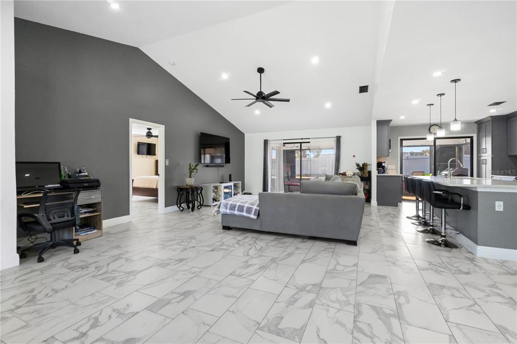 An open-concept living area features a gray accent wall, vaulted ceilings, and white tile flooring — 857 S ATMORE CIRCLE, DELTONA, FL