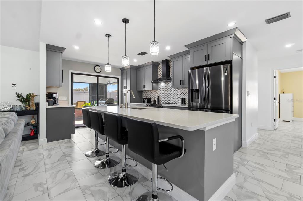A modern kitchen features gray cabinets, a white quartz island, and a chevron-patterned tile backsplash — 857 S ATMORE CIRCLE, DELTONA, FL