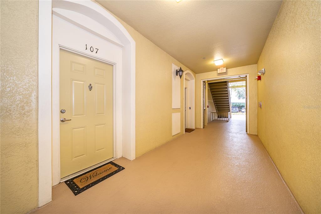 An apartment building hallway features a yellow door numbered 107 and an open stairwell — 3326 ROBERT TRENT JONES DRIVE UNIT 107, ORLANDO, FL