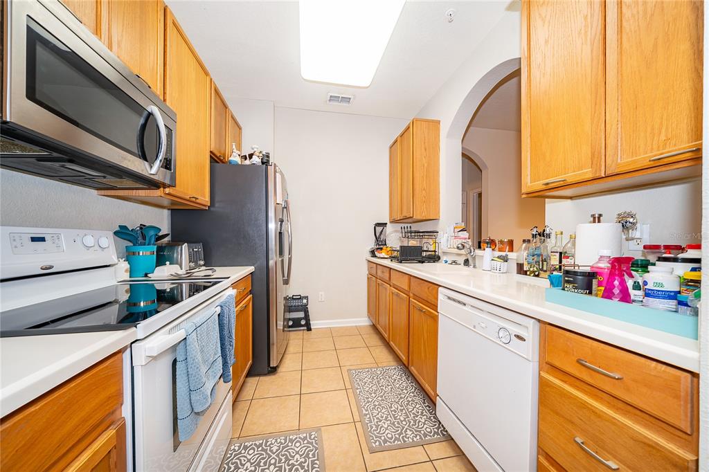 A galley kitchen features oak cabinets, white appliances, and light-colored countertops — 3326 ROBERT TRENT JONES DRIVE UNIT 107, ORLANDO, FL
