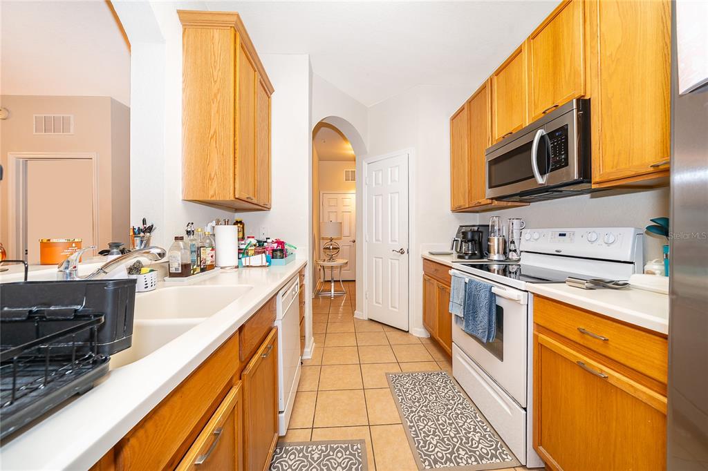 A galley-style kitchen features oak cabinets, white appliances, and light-colored countertops — 3326 ROBERT TRENT JONES DRIVE UNIT 107, ORLANDO, FL