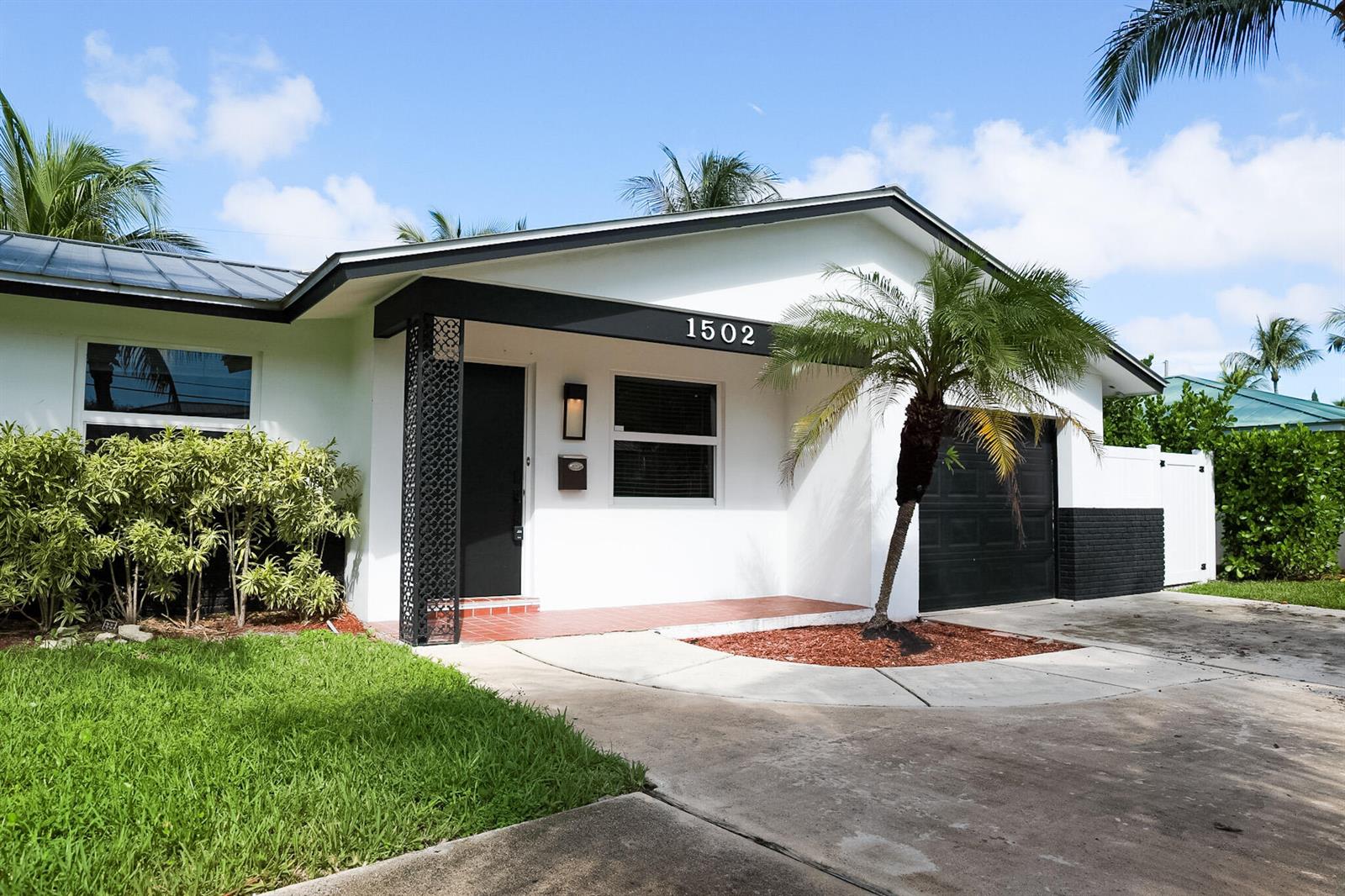 A white single-story house features a black garage door, a front porch, and a palm tree — 1502 NW 4th Avenue, Delray Beach FL 33432, DELRAY BEACH, FL