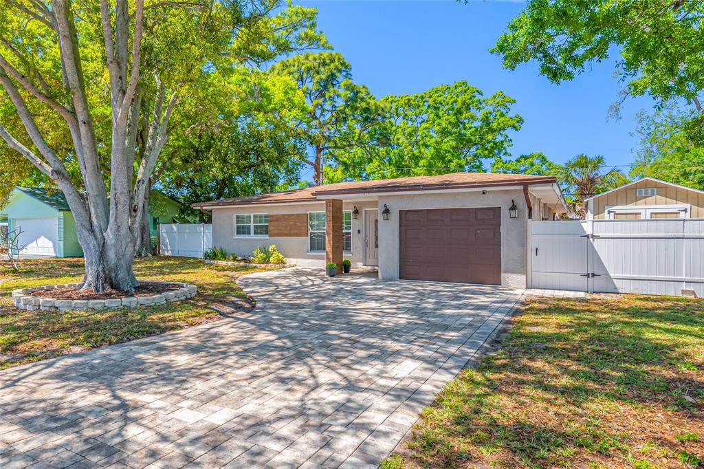 A single-story house with a paved driveway, a brown garage door, and large shade trees — 2212 NE COACHMAN ROAD, CLEARWATER, FL