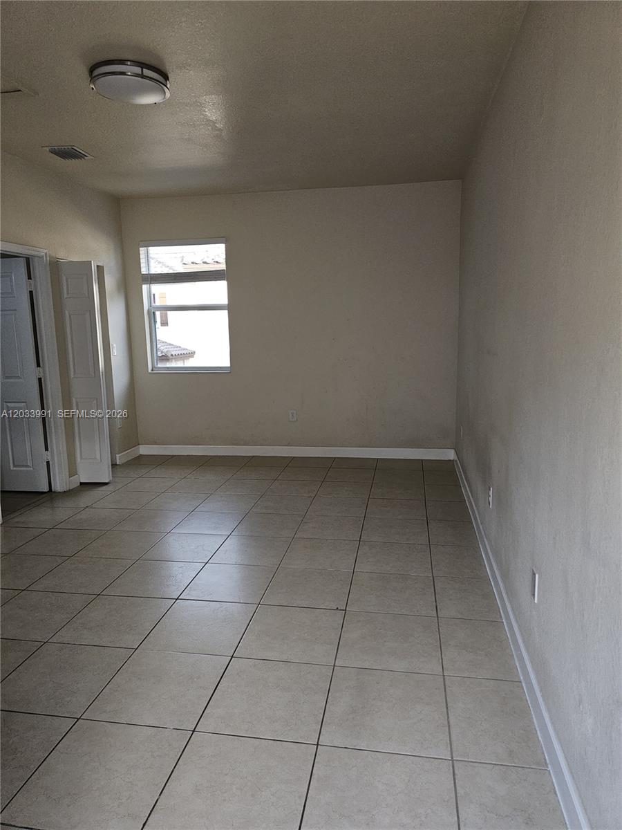 An empty room features beige tile flooring, white walls, and a single window — 17066 SW 95th Ter, Miami FL 33196, MIAMI, FL